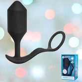 Image of an XL B-Vibe Vibrating Cock Ring - Snug & Tug in black, featuring a looped handle, set against a vibrant bokeh background. The product box is visible in the bottom right corner, displaying the same design and brand.